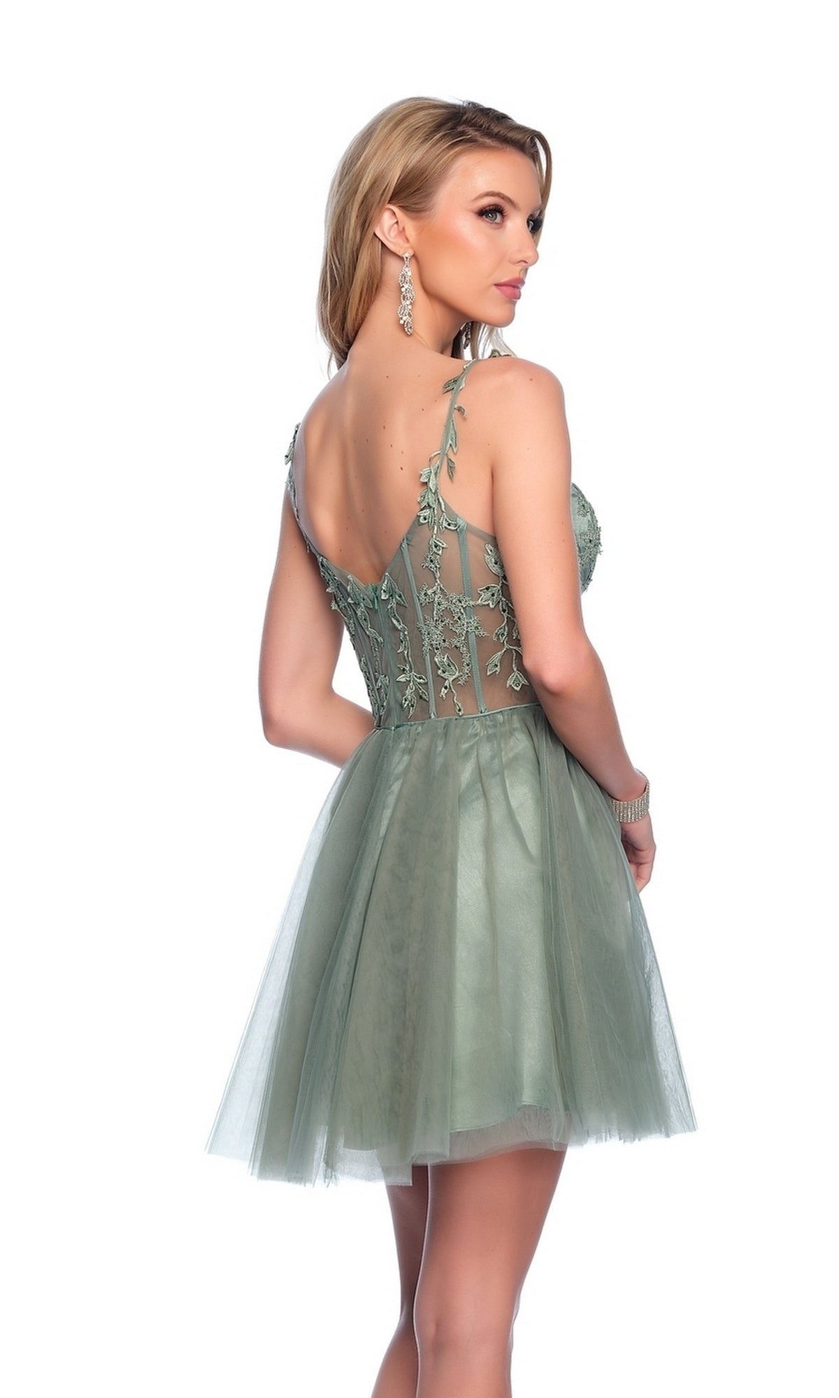 A woman stands looking over her shoulder, wearing the Dave & Johnny 11920 sage green homecoming dress with floral lace details, a corset bodice, and a tulle A-line skirt.
